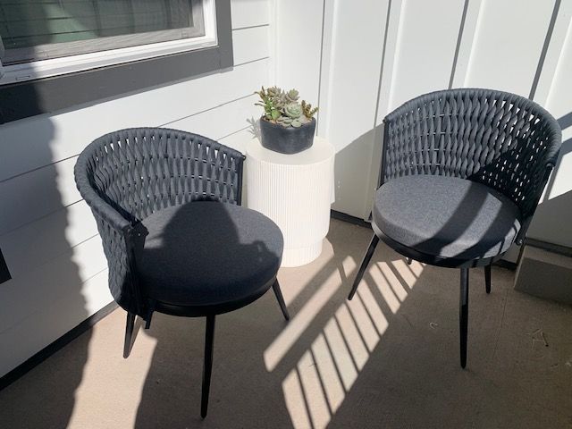 Two dark gray woven chairs with cushions and a small side table holding a potted plant on a balcony.