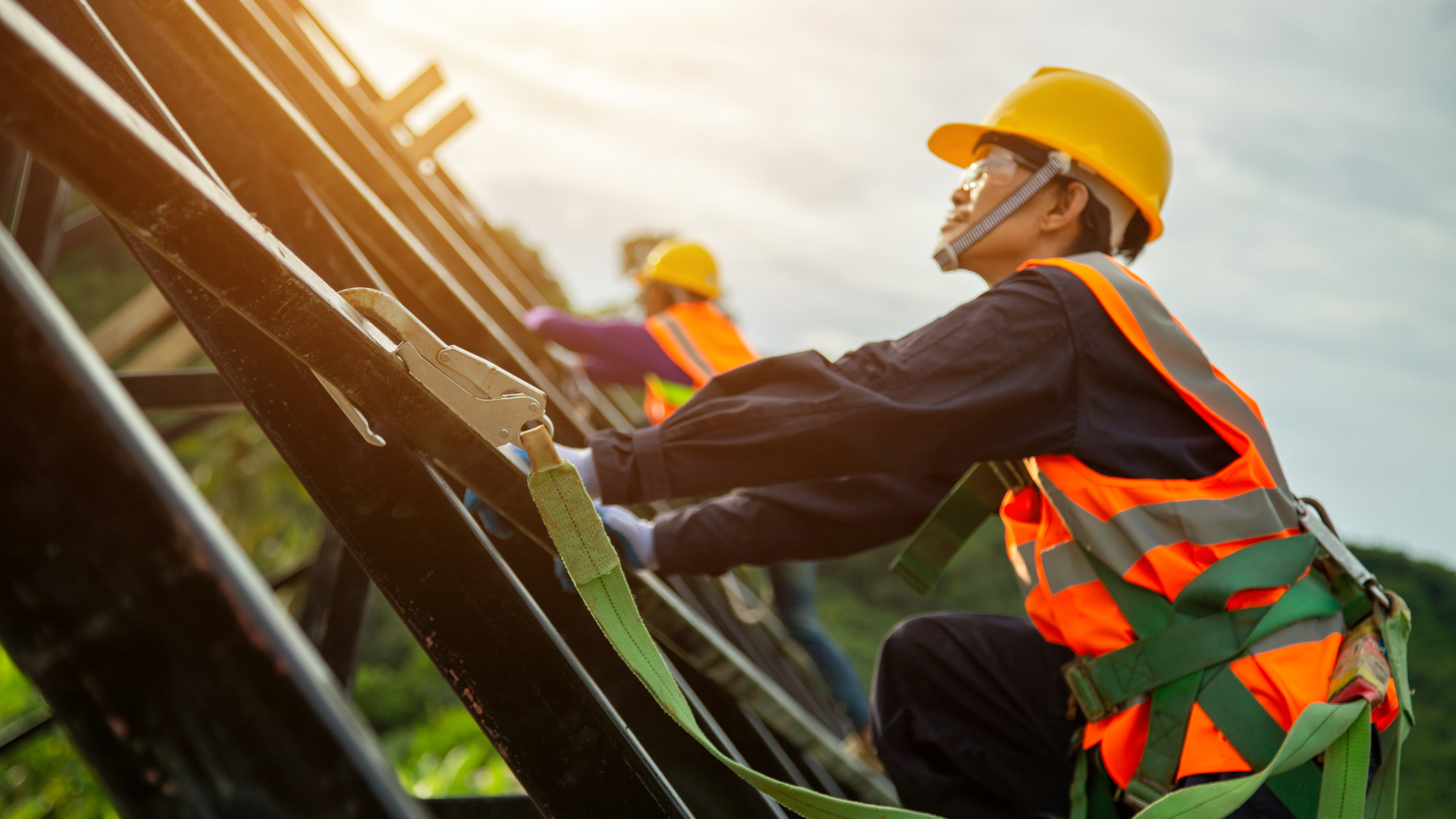 Construction workers wearing safety harnesses and helmets on a roof, securing beams.