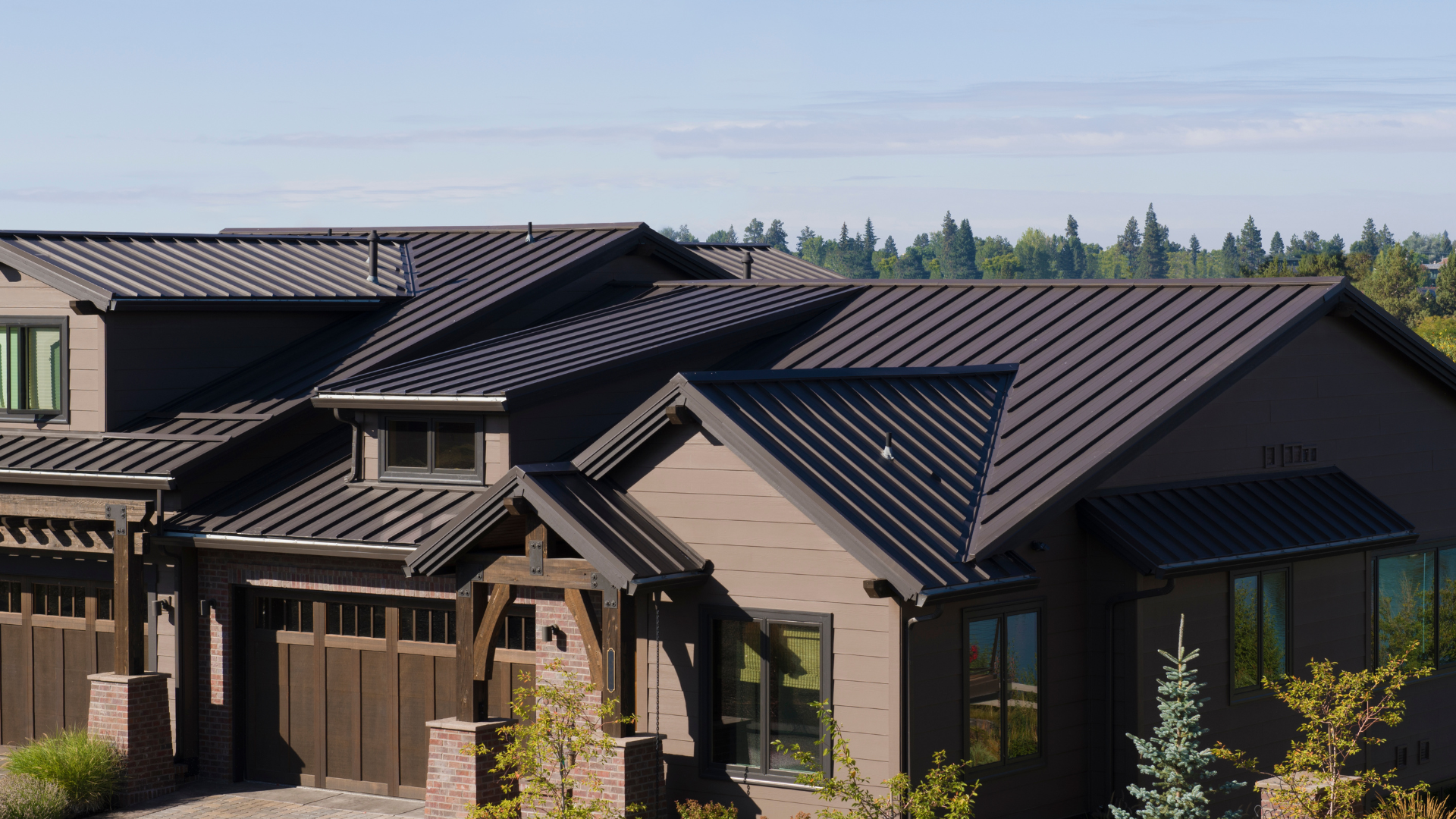 Brown house with multiple roof sections and a wooden garage door against a blue sky.