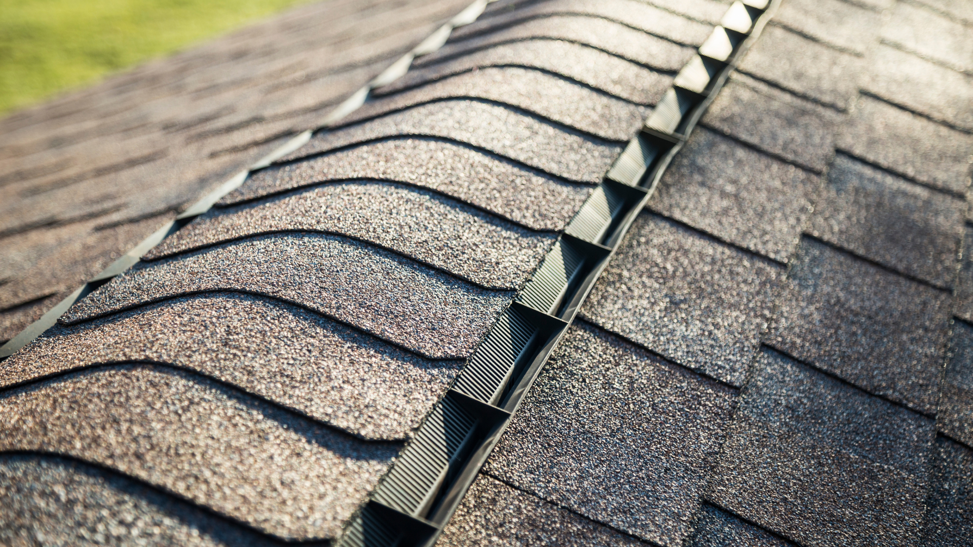 Close-up of a brown shingle roof with a dark, ridged valley between two sloping sections.