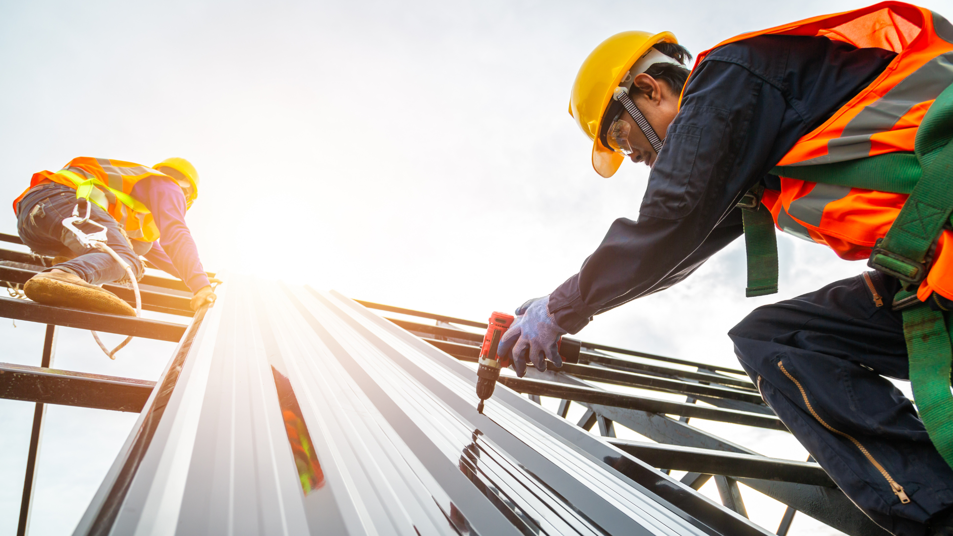 Construction workers installing metal roof panels, wearing safety gear and hard hats.