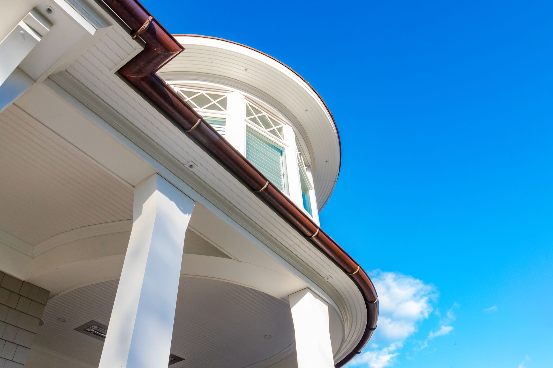 White porch with brown gutters against a bright blue sky.