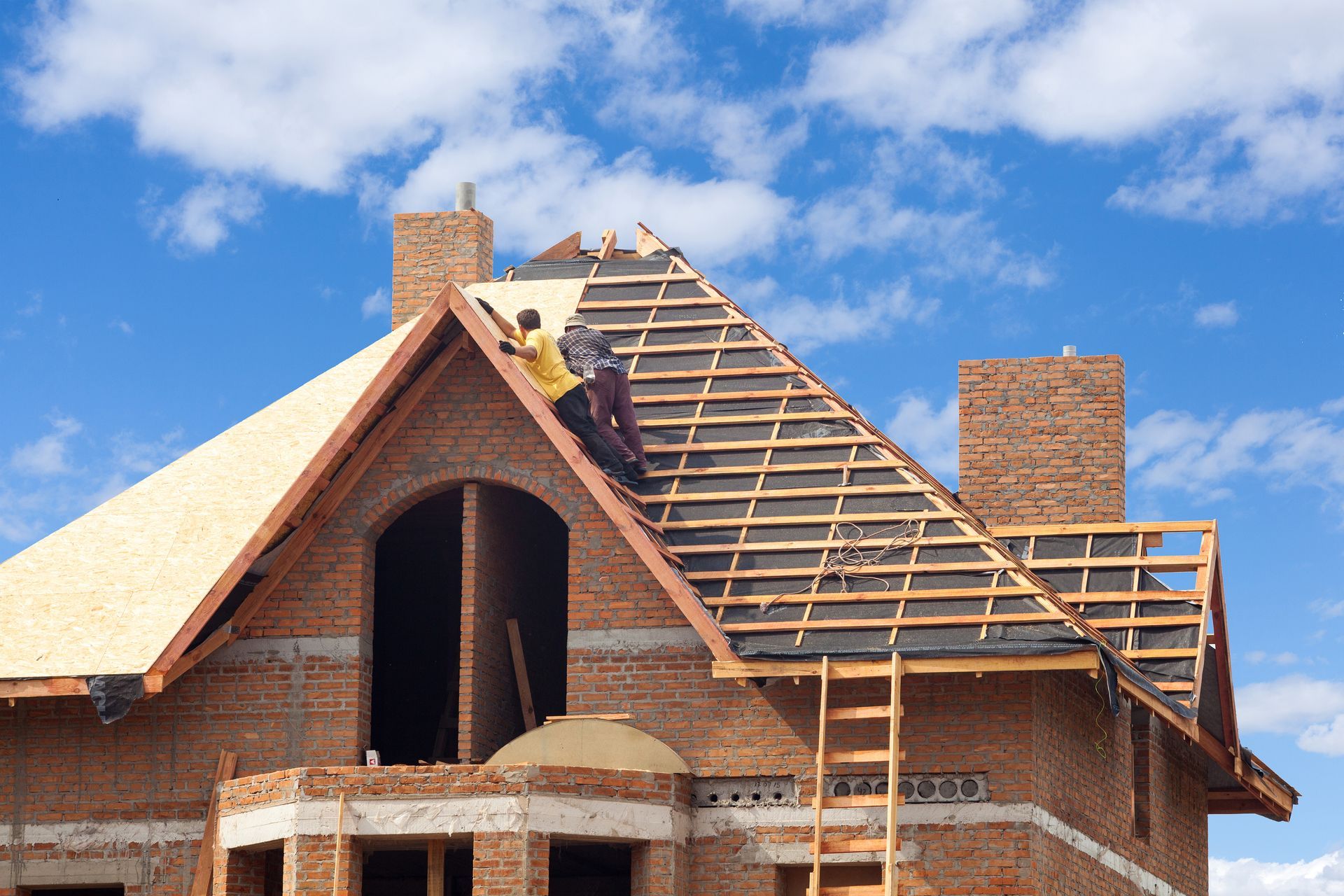 Workers installing roof on brick house under construction, blue sky.