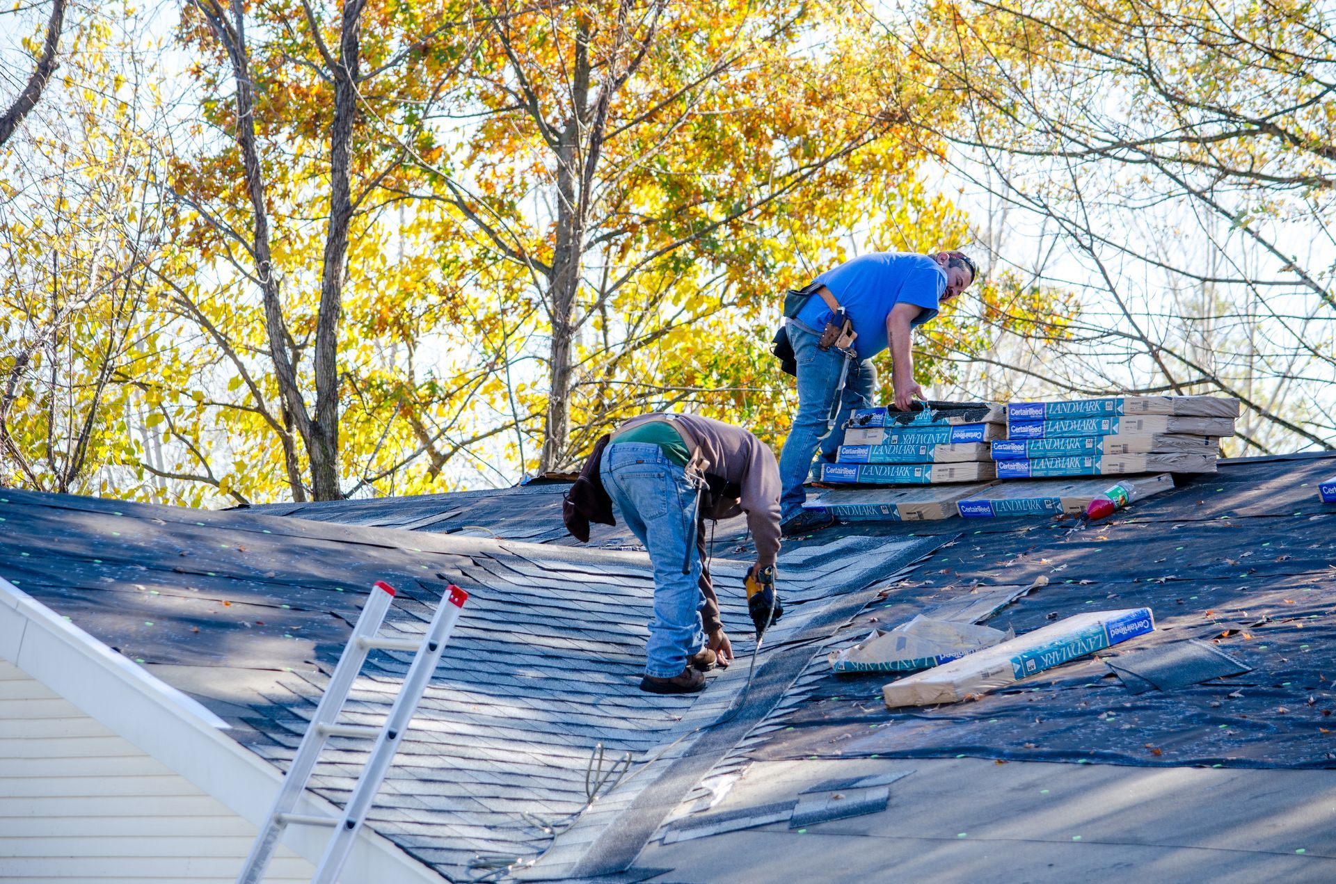 Two roofers installing shingles on a house roof on a sunny day.