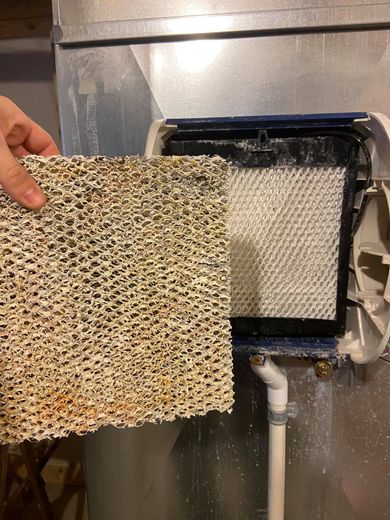 Hand holding a dirty, porous filter next to an air humidifier filter.