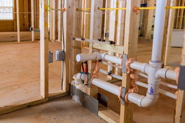 Wooden framing with installed white plumbing pipes and electrical boxes in a new construction space.
