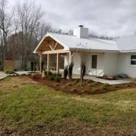 White house with a covered front porch, snow on the roof, and a grassy yard on a cloudy day