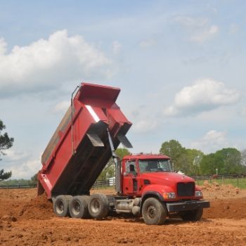 Red dump truck tipping its bed to unload dirt at a construction site