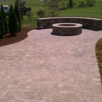 Brick patio with a curved stone seating wall and round fire pit in a landscaped backyard.