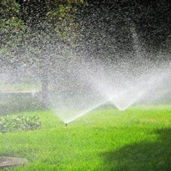 Sprinklers watering a bright green lawn in sunlight, creating a misty spray.