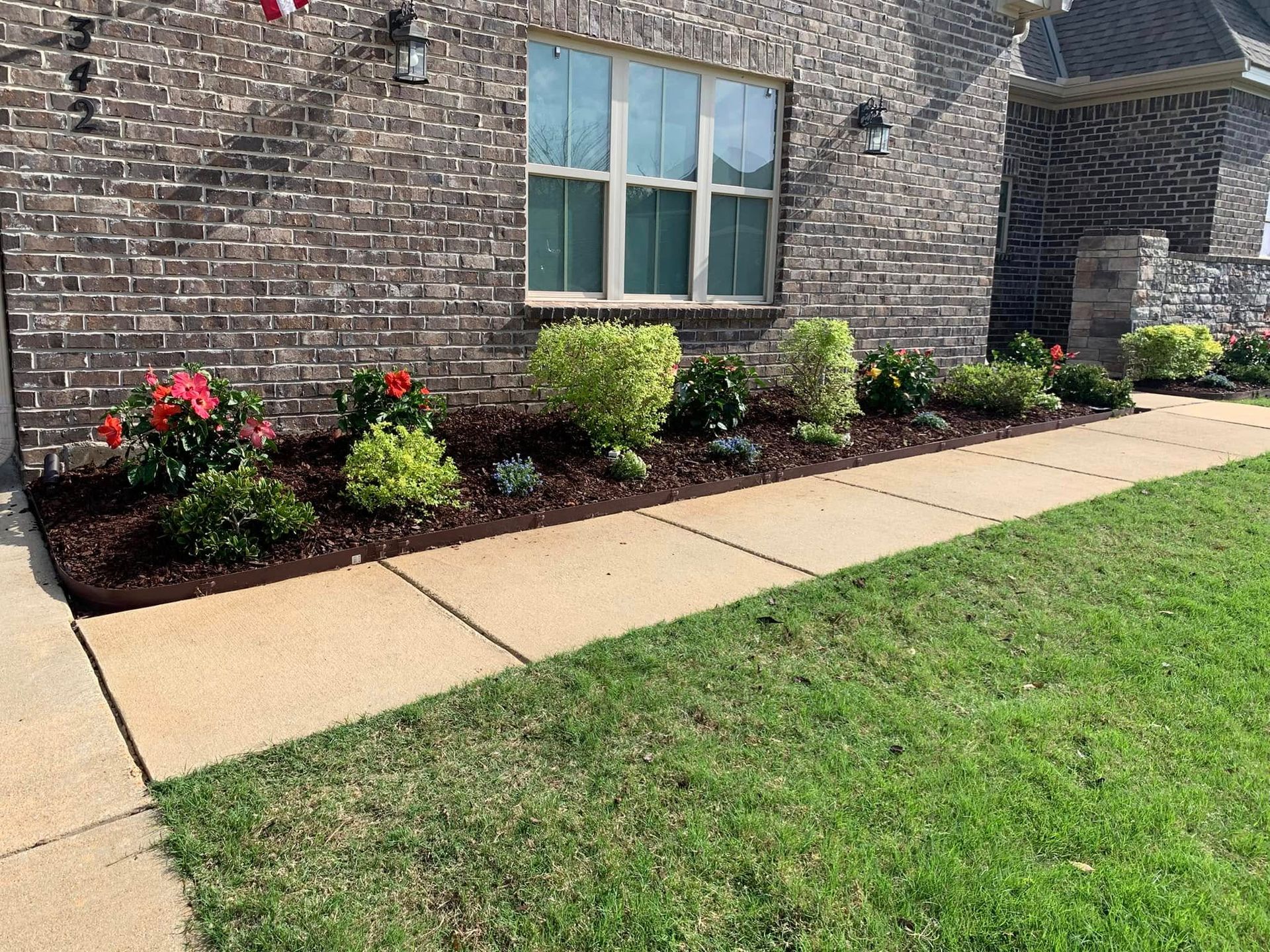 A brick house with a sidewalk and flowers in front of it.