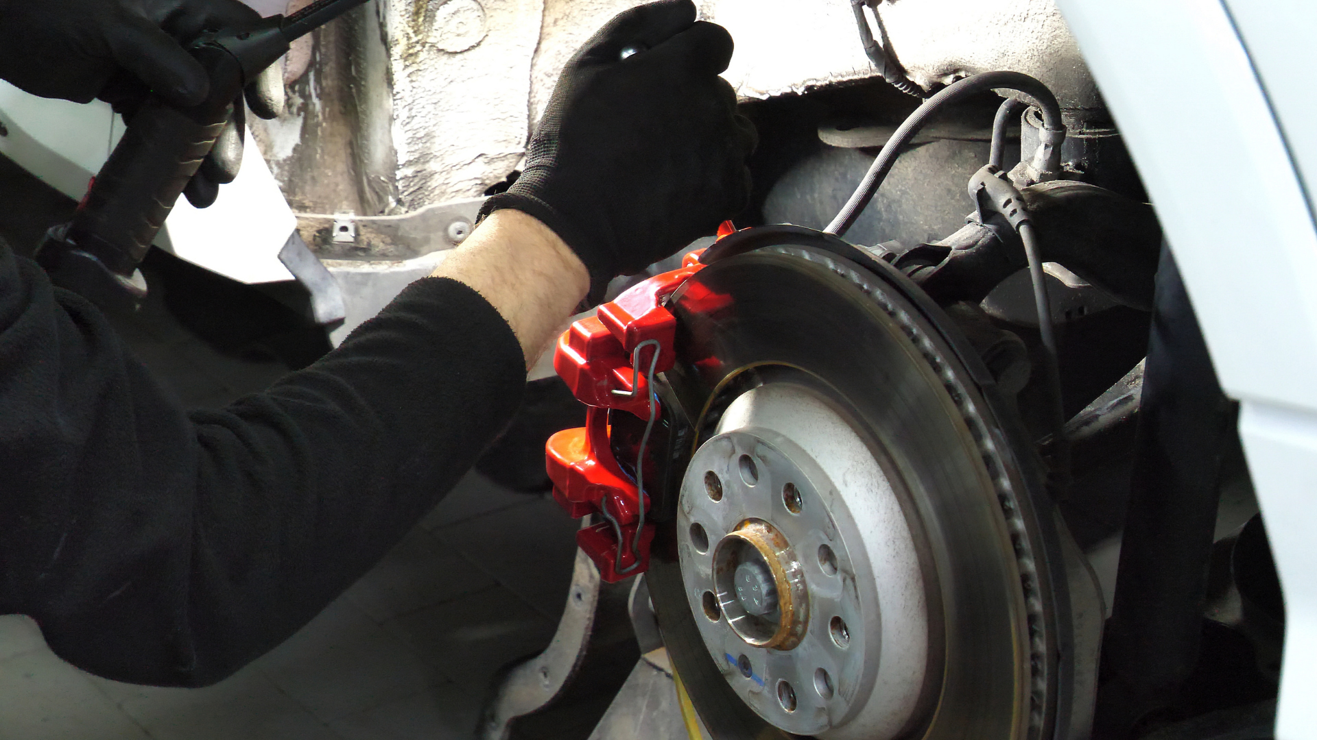 Person wearing black gloves working on a car's brake system, near a red brake caliper.