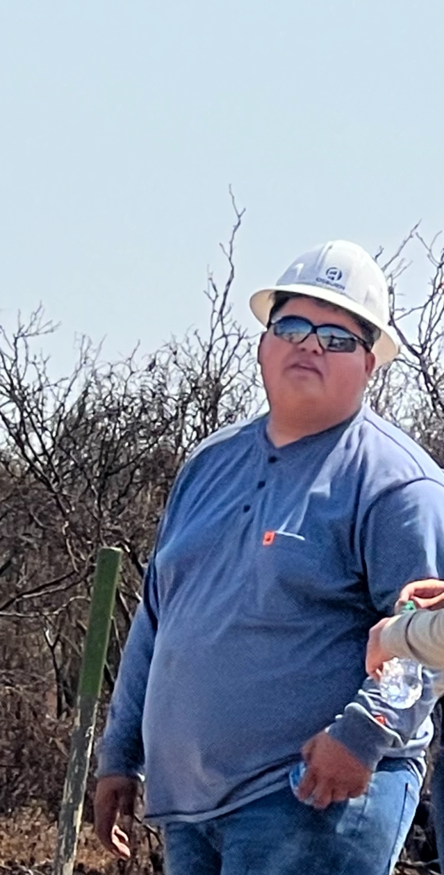A man wearing a hard hat and sunglasses is standing in a field.