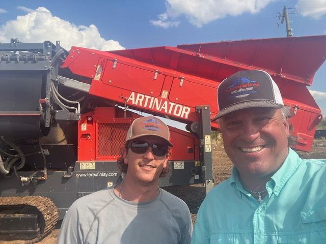 Two men are posing for a picture in front of an artinator machine