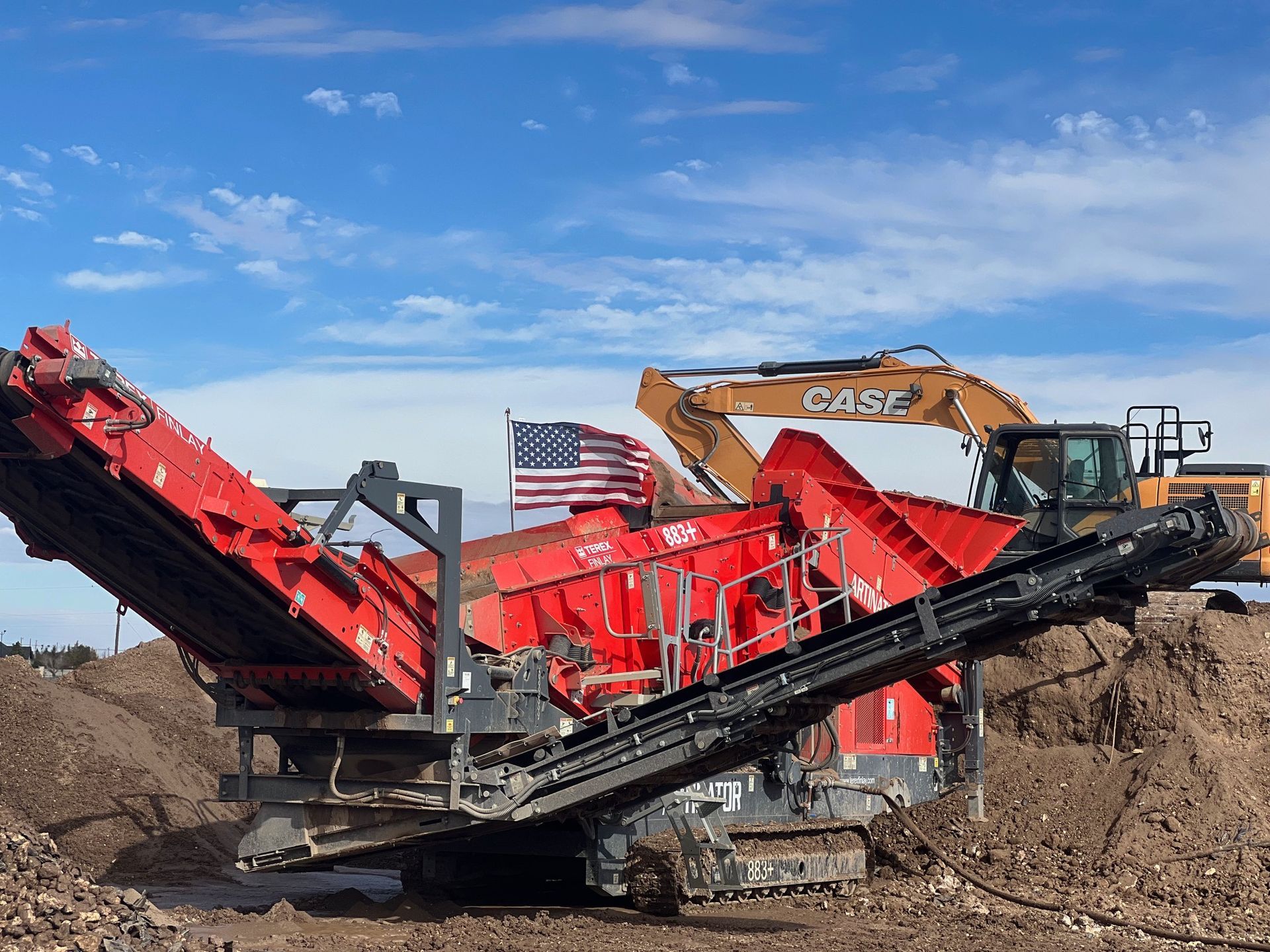 A large red machine is sitting in the middle of a dirt field.