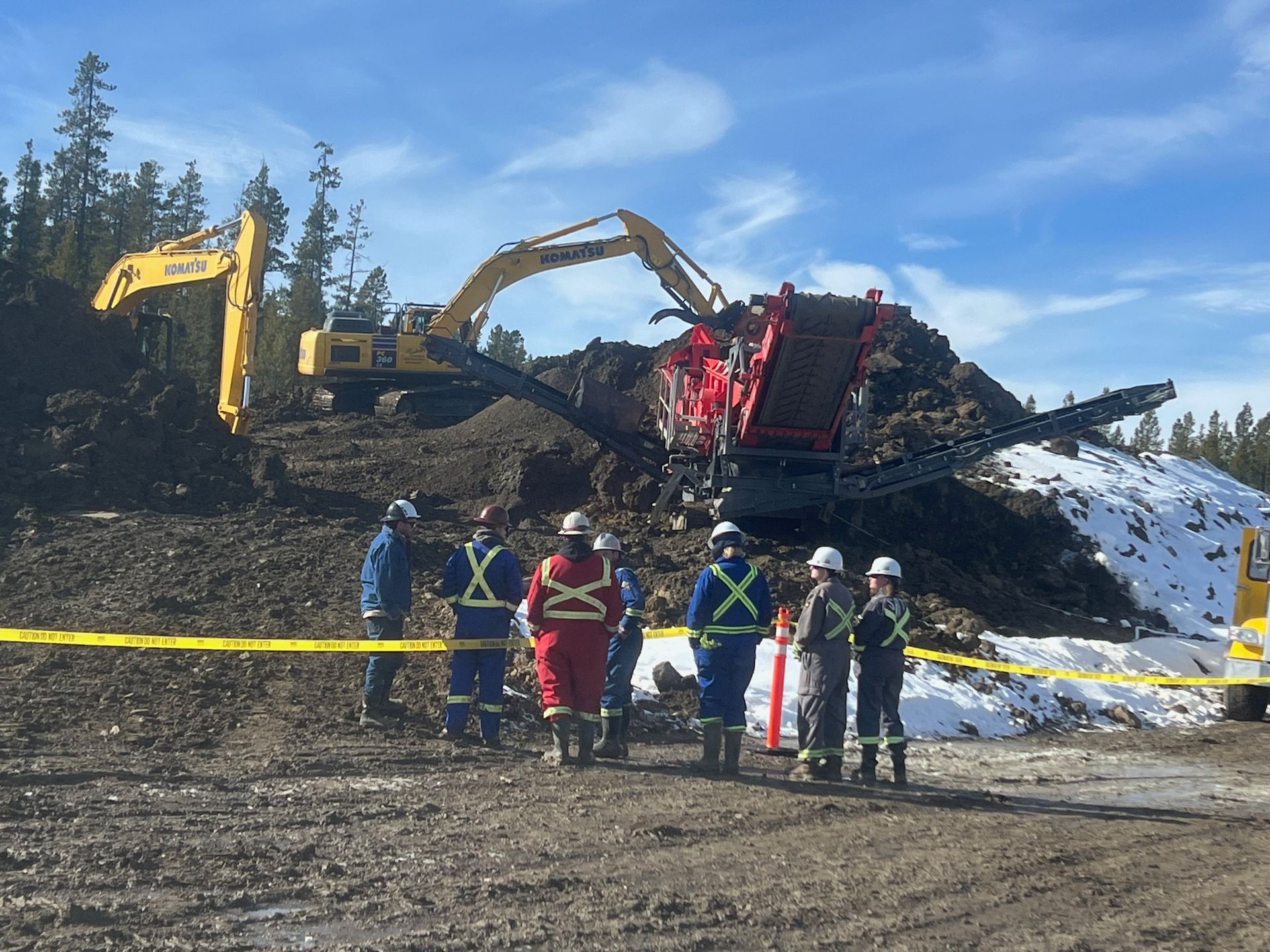 A group of construction workers are standing in front of a large pile of dirt.
