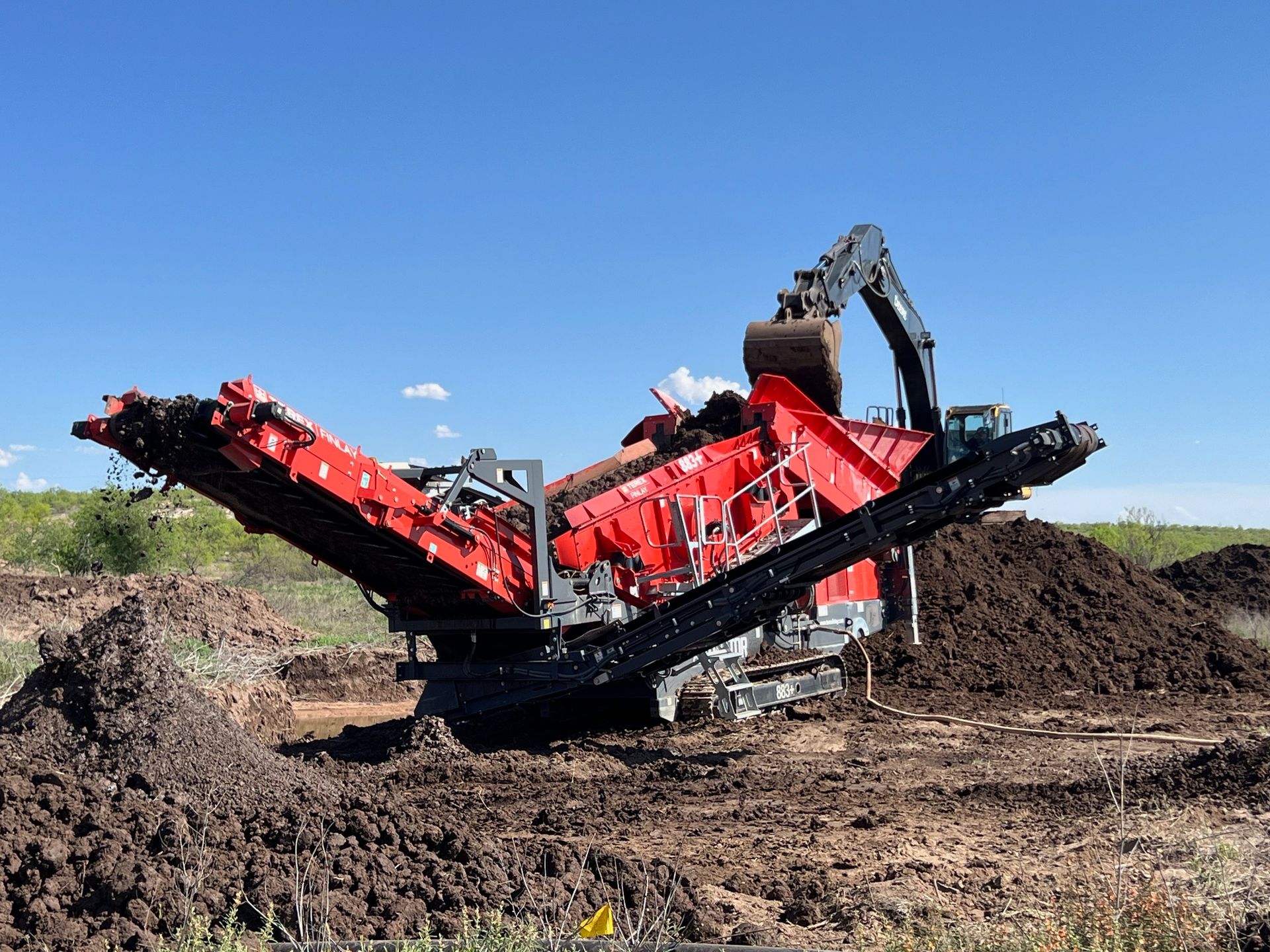 A red and black machine is sitting in a pile of dirt.