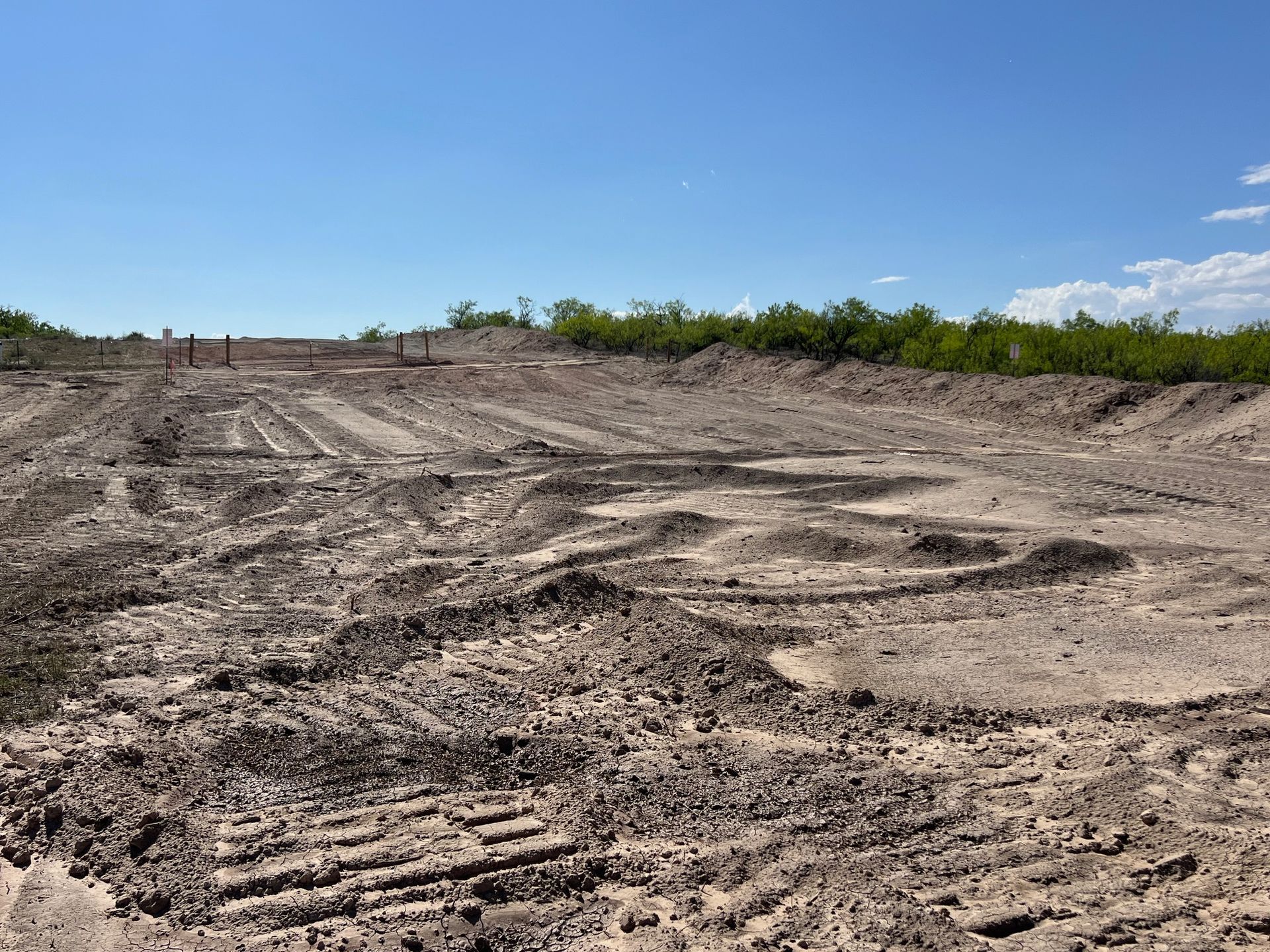 A dirt field with trees in the background and a blue sky
