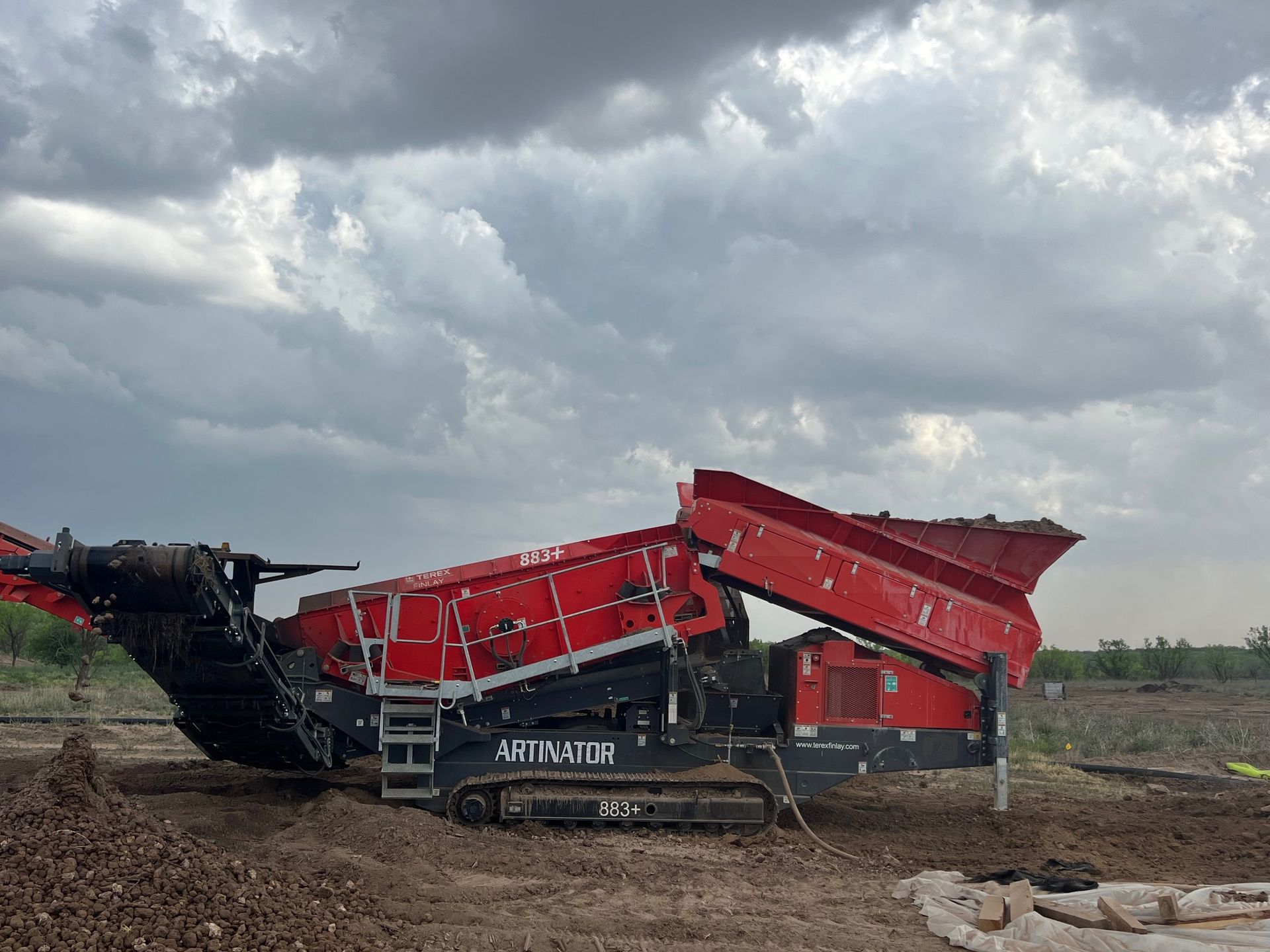 A large red and black machine is sitting in the middle of a dirt field.