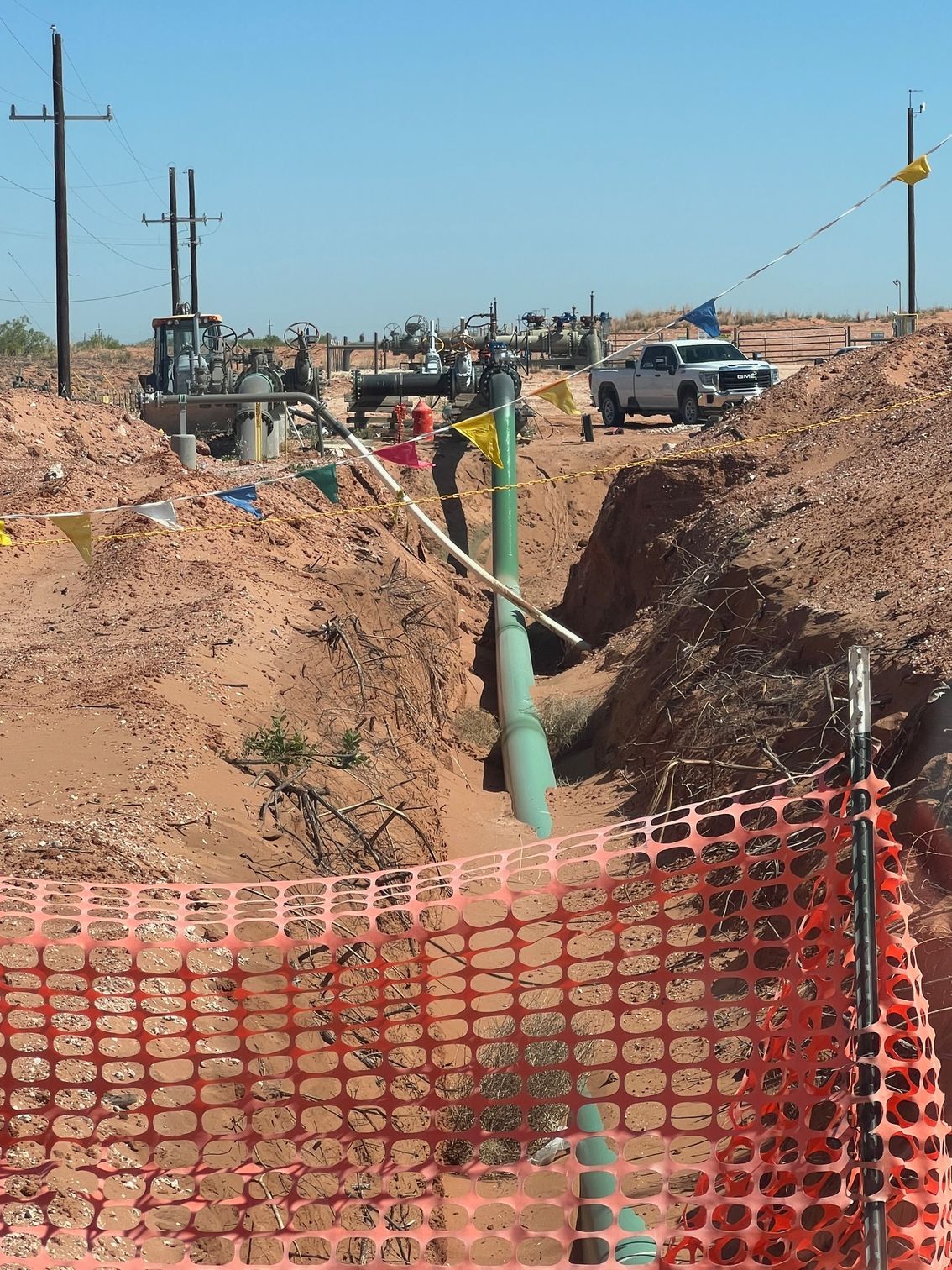 A green pipe is being installed in the dirt behind an orange fence.