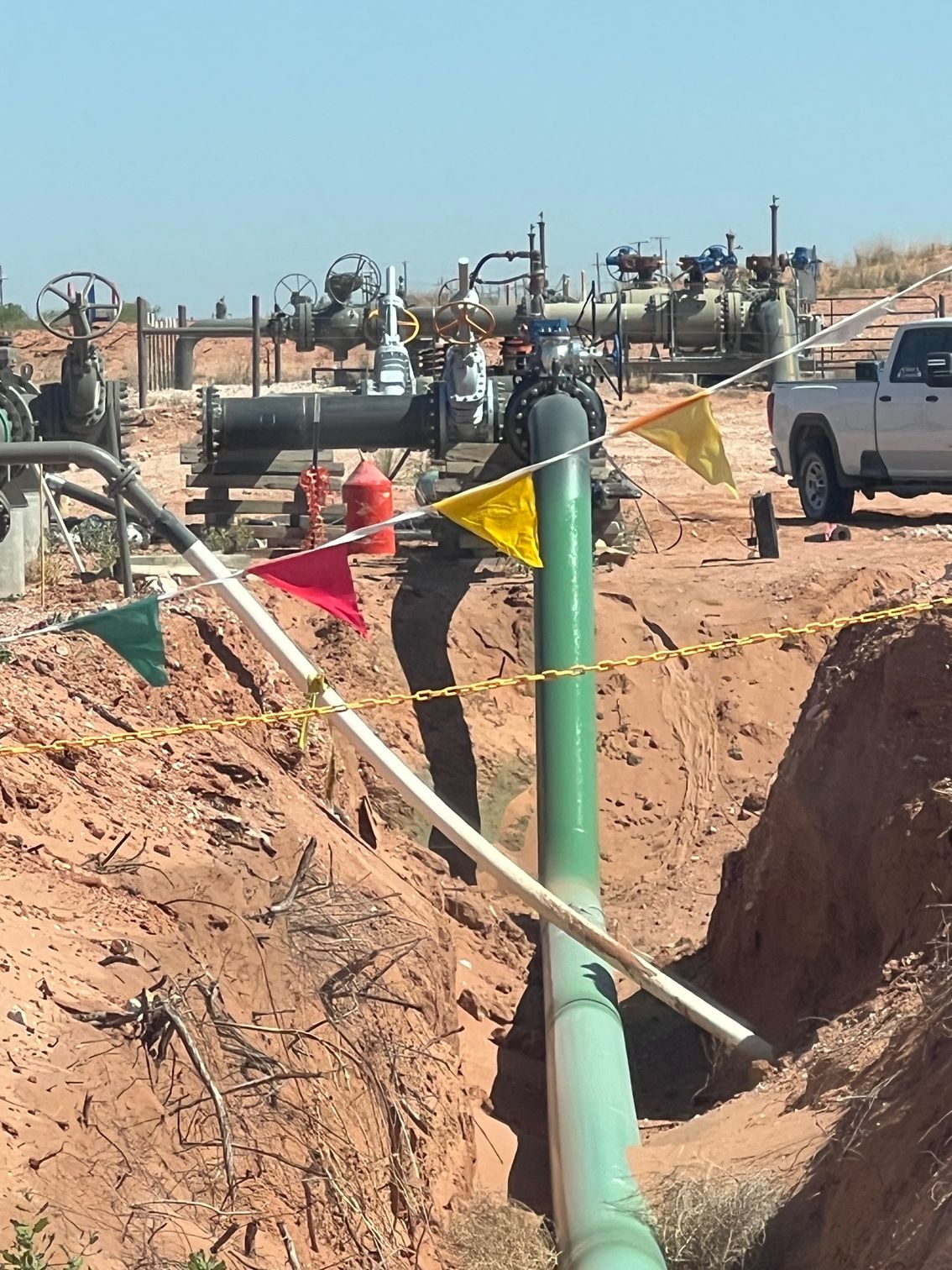 A white truck is parked next to a green pipe in the dirt.