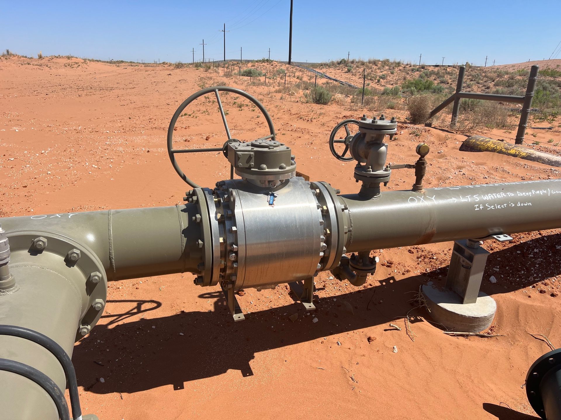 A pipe with a valve on it is in the middle of a desert.