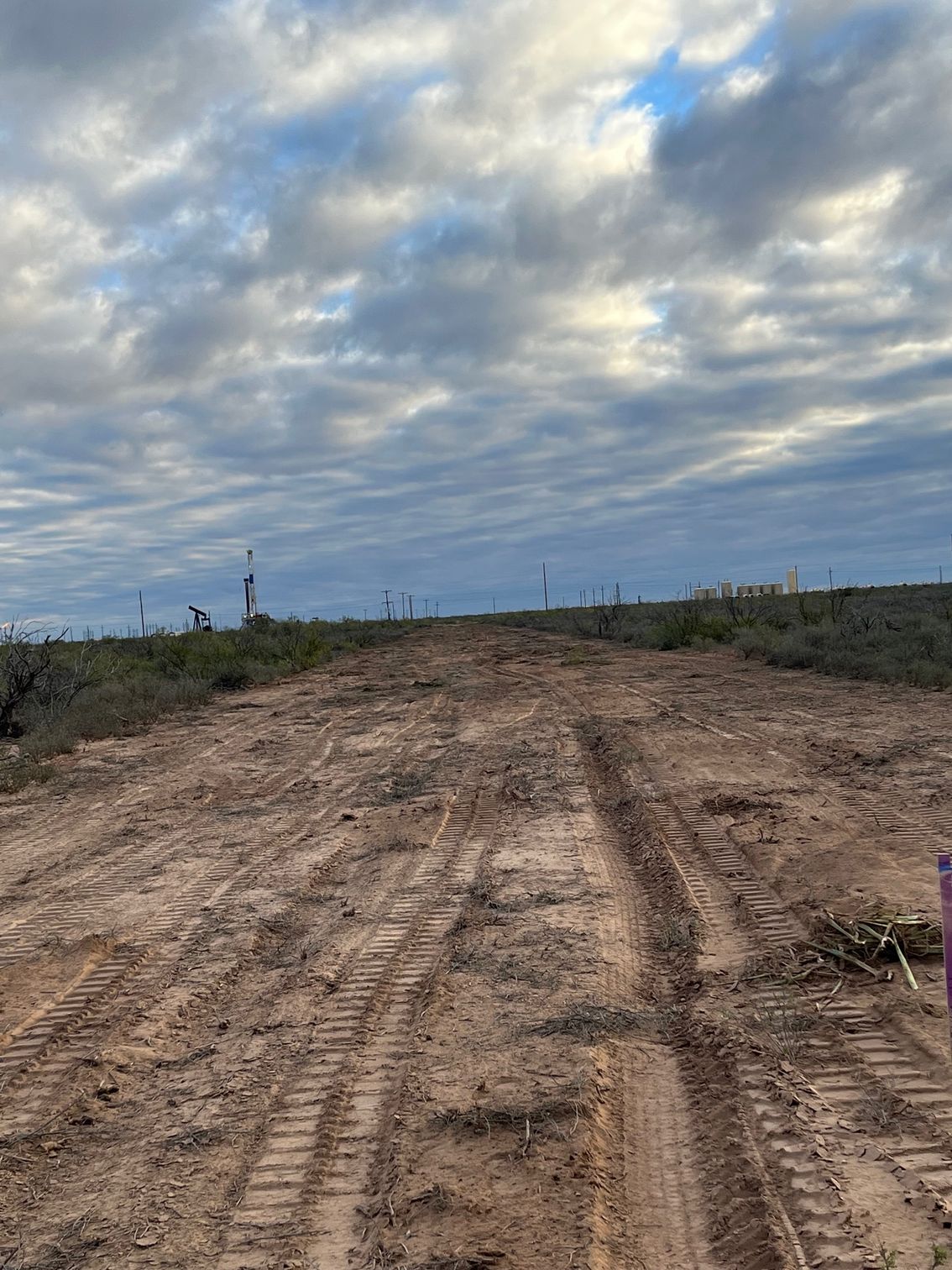 A dirt road with tire tracks on it and a cloudy sky in the background.