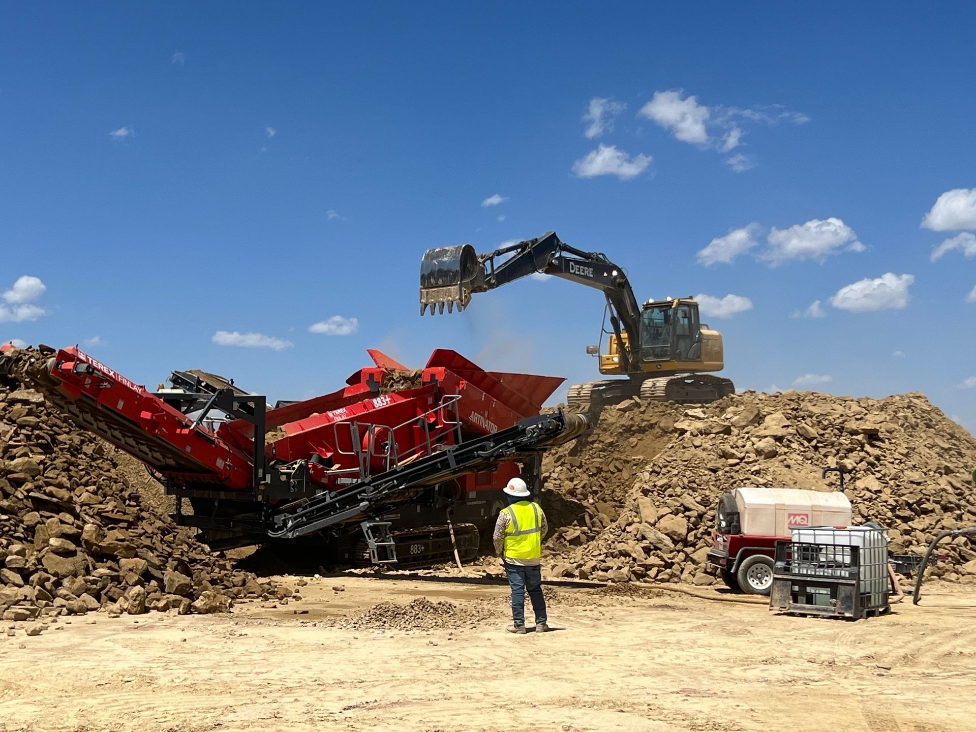 A man in a yellow vest is standing in front of a large pile of dirt.