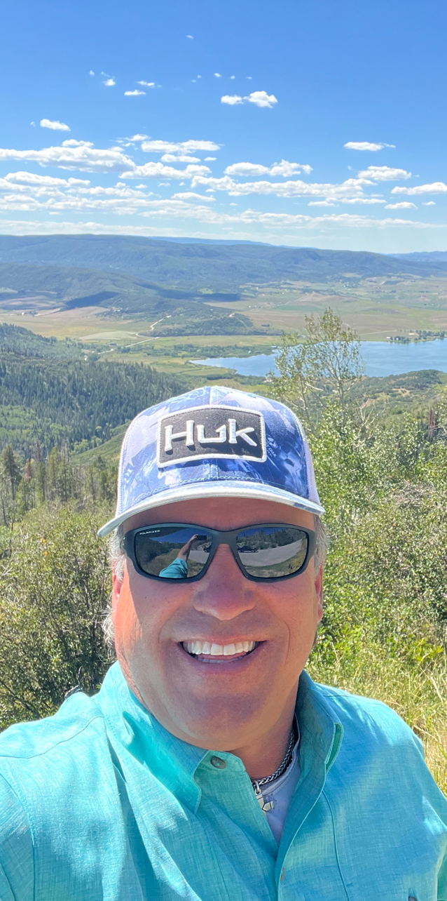 A man wearing a hat and sunglasses is standing on top of a hill.