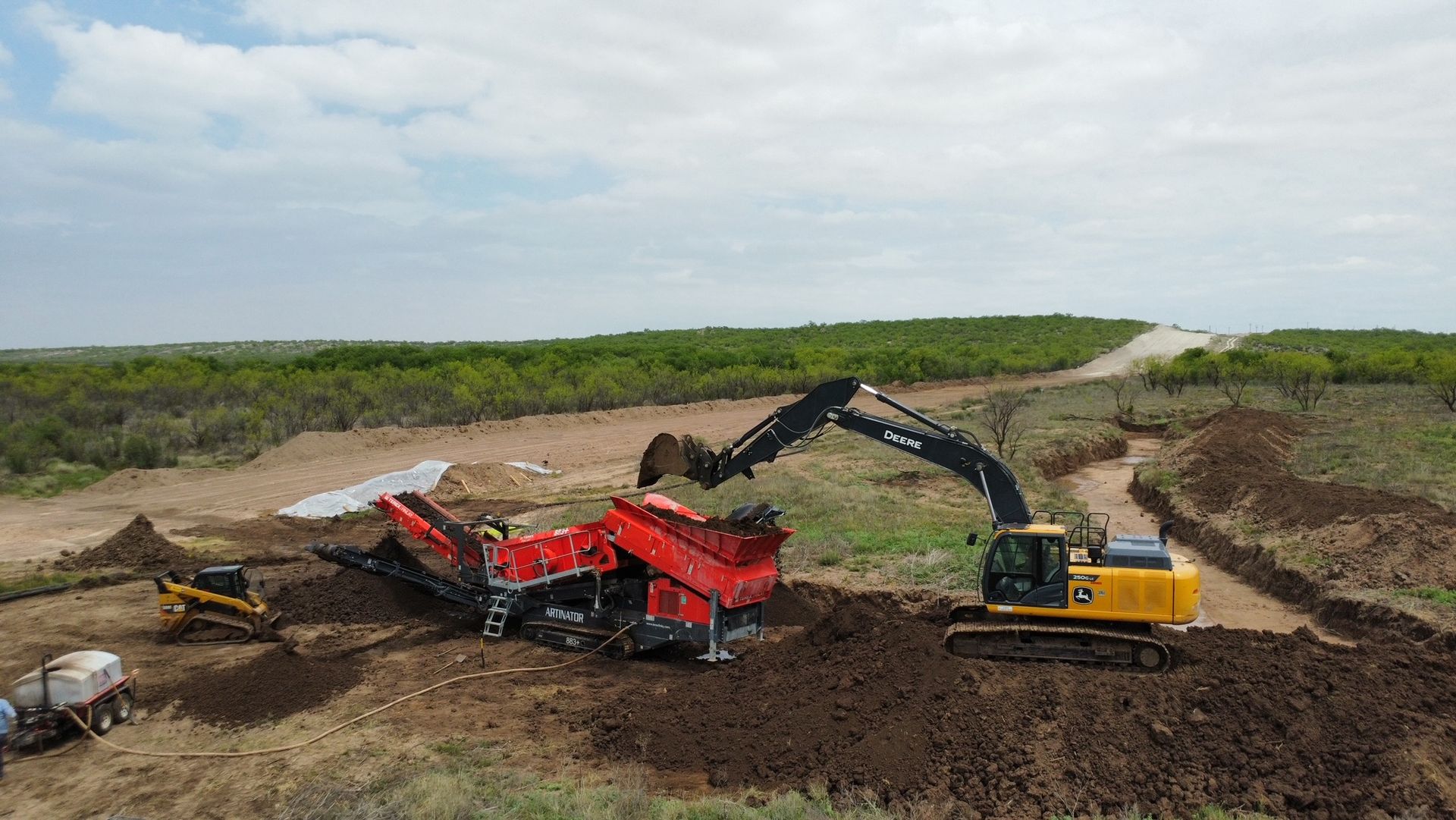 An aerial view of a large excavator moving dirt in a field.