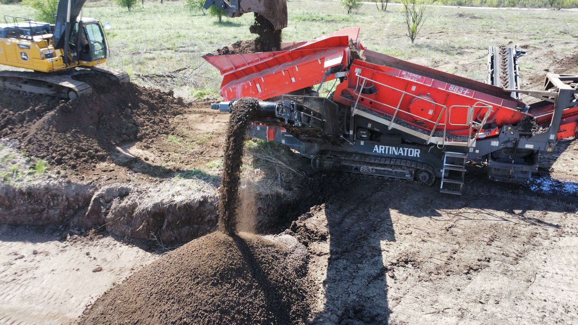 A large excavator is loading dirt into a dumpster.