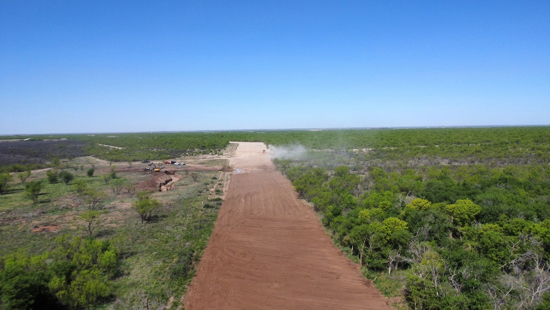 An aerial view of a dirt road going through a lush green field.