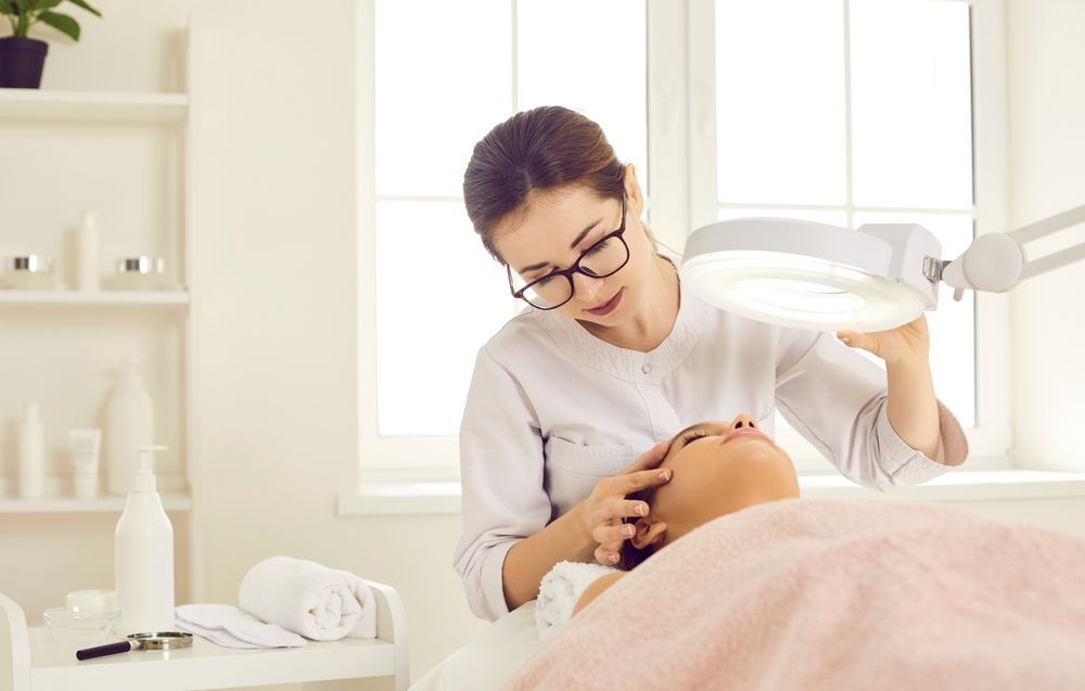 A woman is looking at a woman 's face under a magnifying glass in a beauty salon.