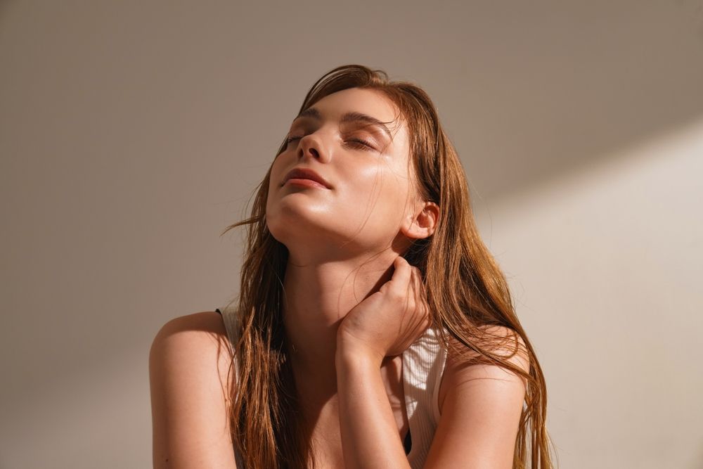 A woman is looking up at the sun with her eyes closed.