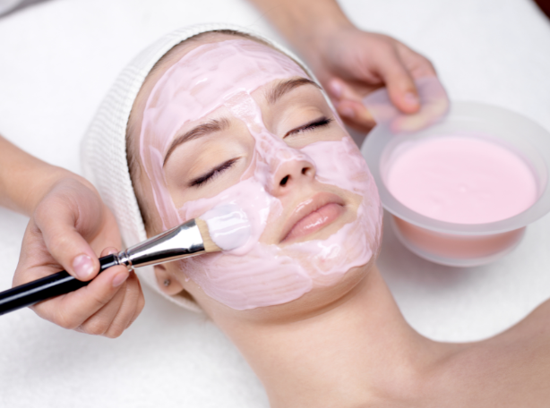 A woman is getting a pink mask on her face.