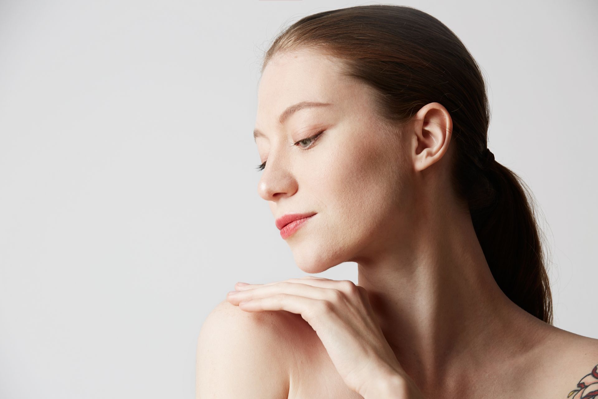 A woman with a tattoo on her shoulder is touching her face.