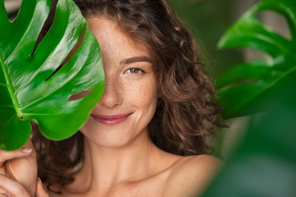 A woman is covering her face with a green leaf.