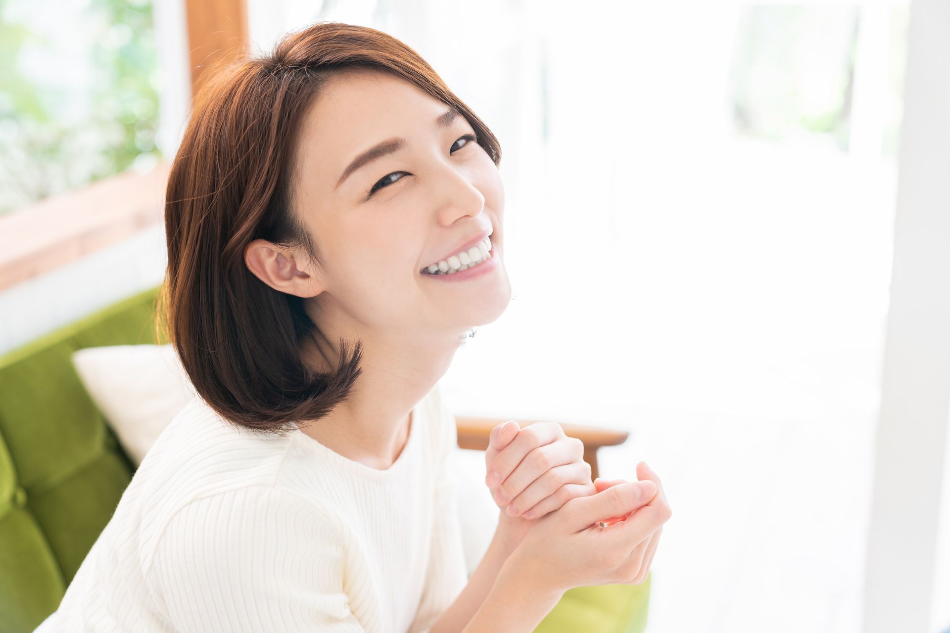 A woman is smiling while sitting on a couch in a living room.