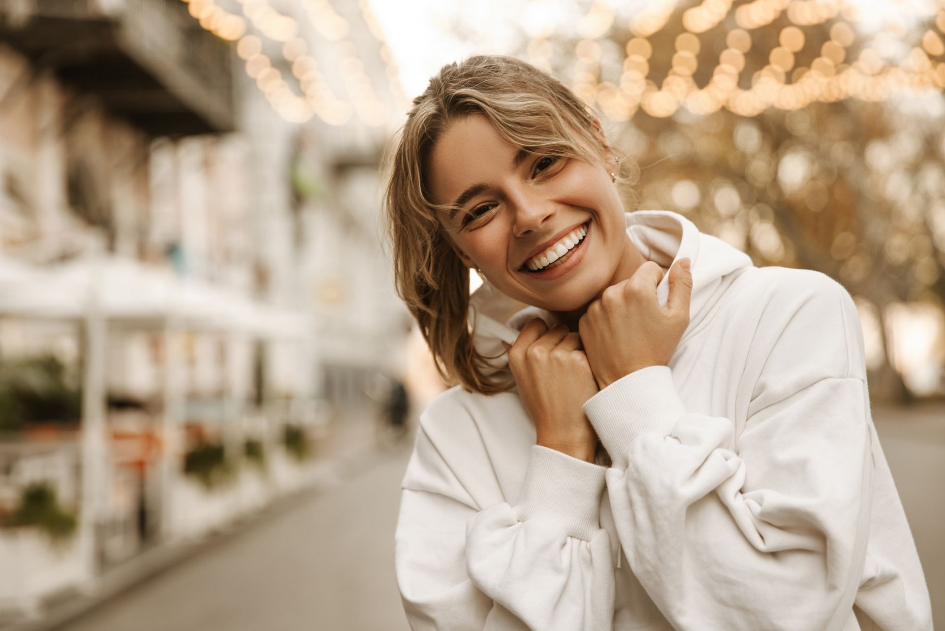 A woman in a white hoodie is smiling and looking at the camera.