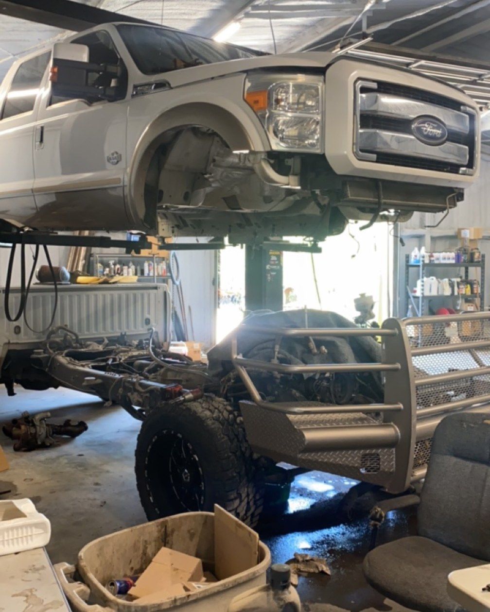 White Ford truck on a lift in a garage, undergoing repair. The chassis is detached.