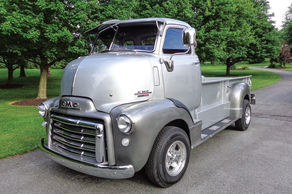 Silver GMC pickup truck on a paved road; trees in the background, clear day.