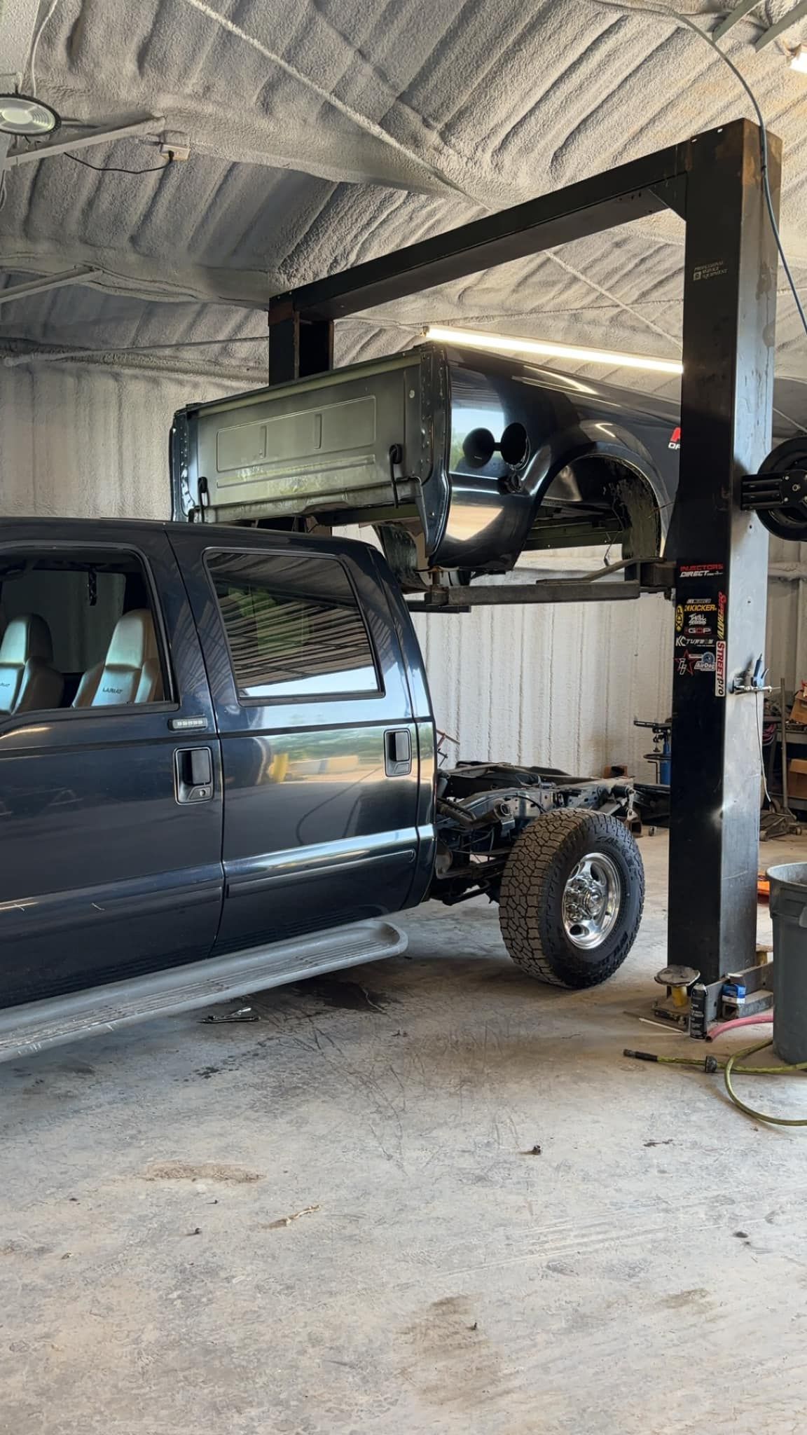 Truck cab raised on a lift in a garage, revealing chassis.