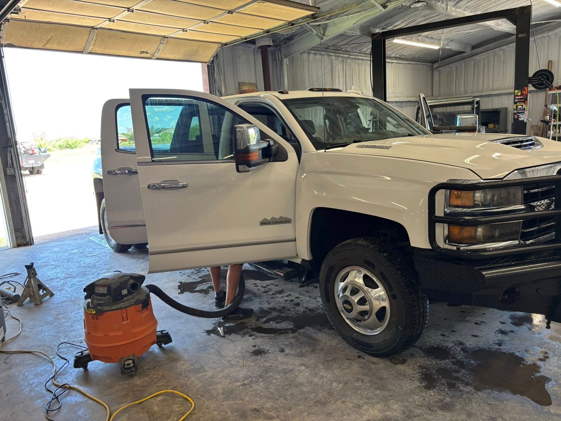 White pickup truck with open door being cleaned in a garage. An orange vacuum cleaner sits nearby.