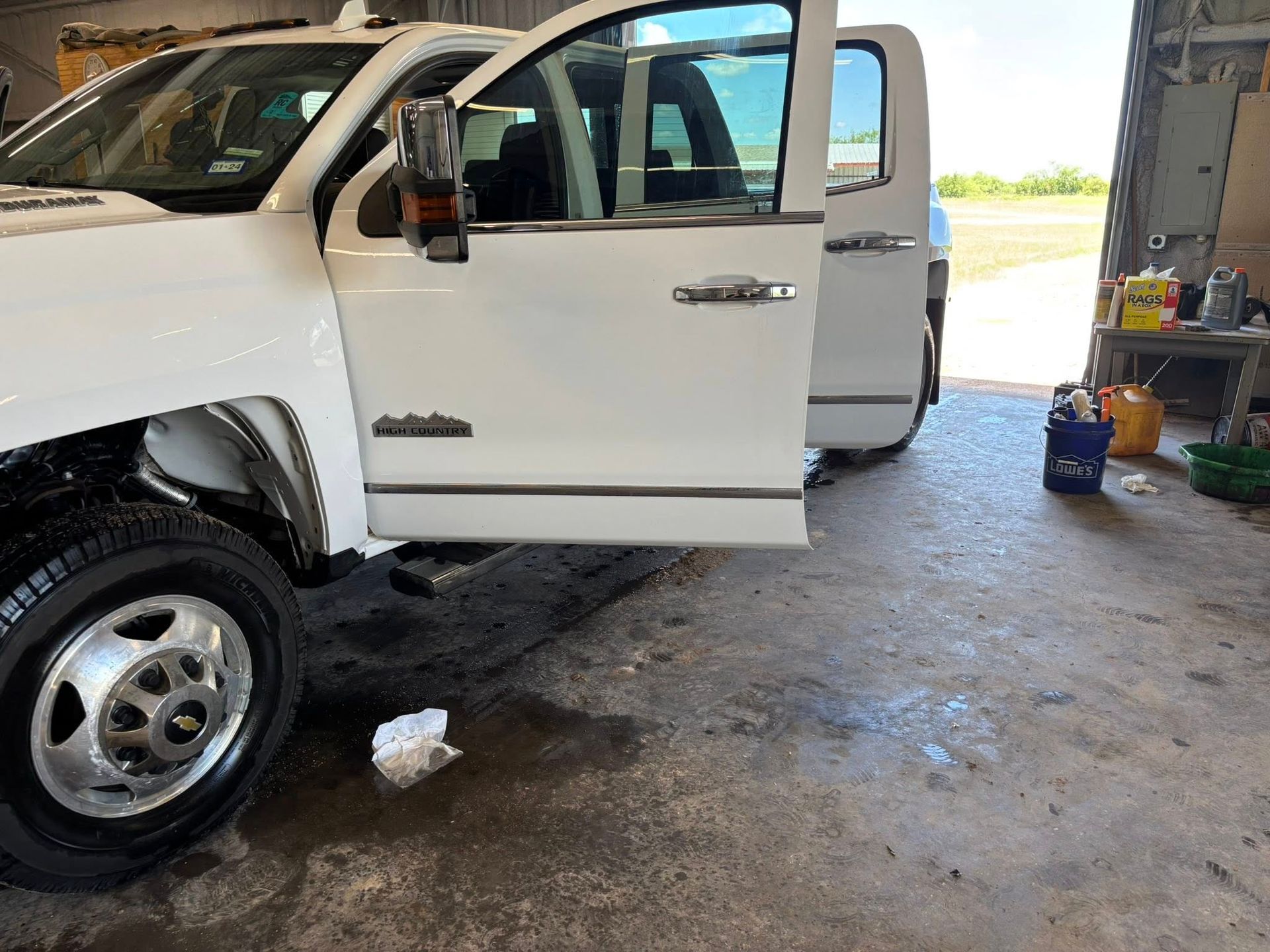 White pickup truck with open door, parked on wet concrete.