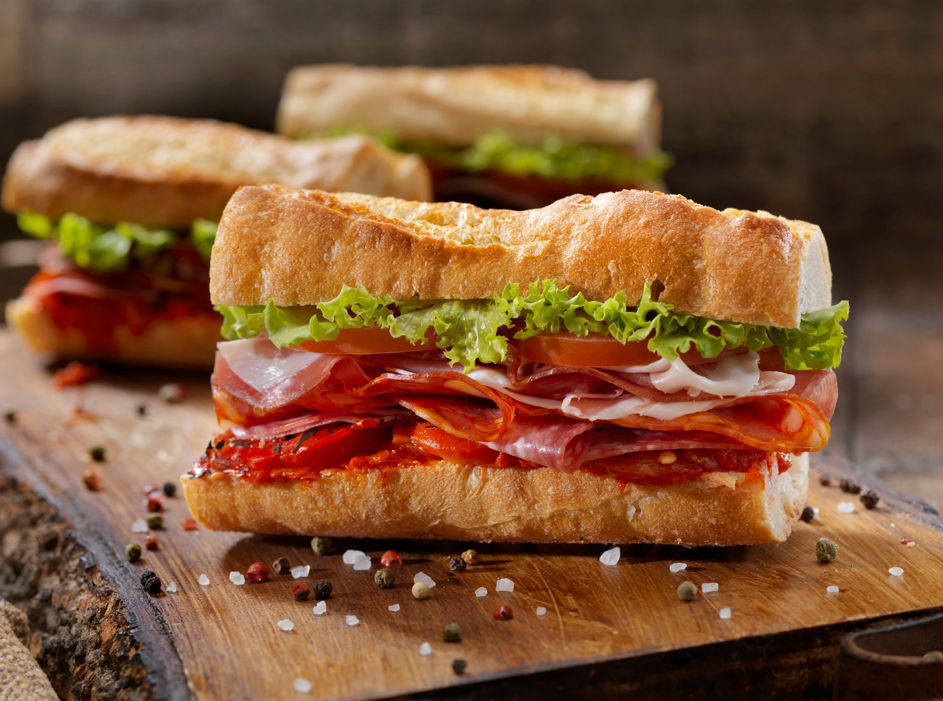 Panini con vari tipi di carne, lattuga e pomodori su un tagliere di legno.