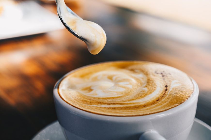 Tazza di caffè con schiuma vorticosa, cucchiaio che raccoglie la schiuma.