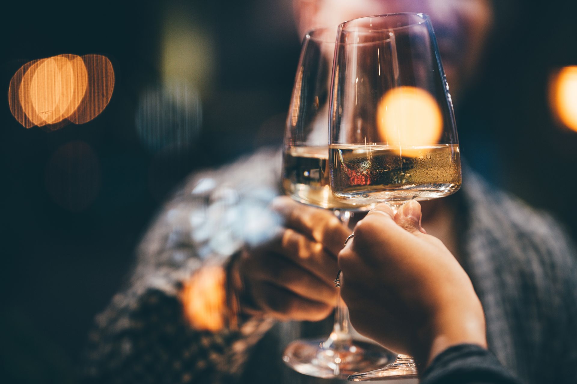 Due mani che brindano con bicchieri di champagne. Luci bokeh sullo sfondo.