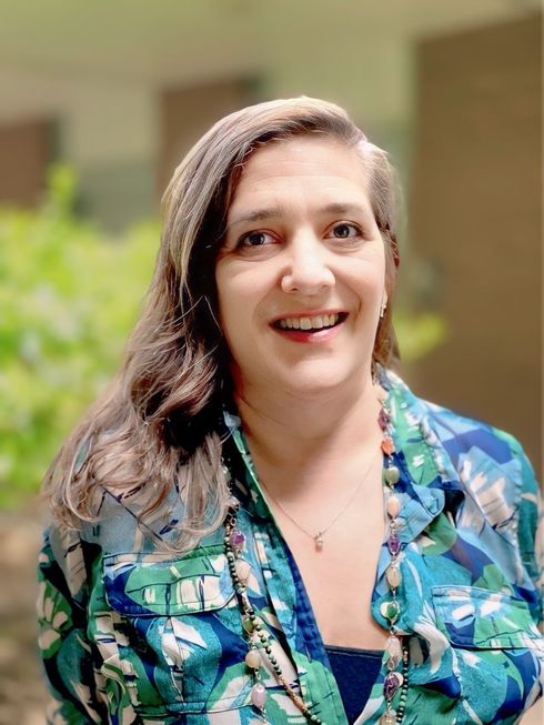 A woman wearing glasses and a white shirt is smiling for the camera.