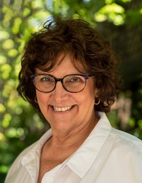 A woman wearing glasses and a white shirt is smiling for the camera.