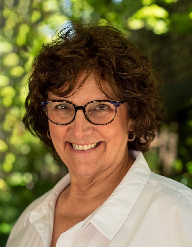 A woman wearing glasses and a white shirt is smiling for the camera.